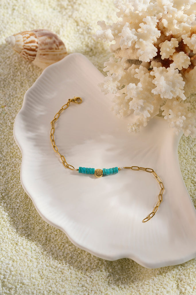 Gold bracelet with turquoise beads on a white shell with coral in the background